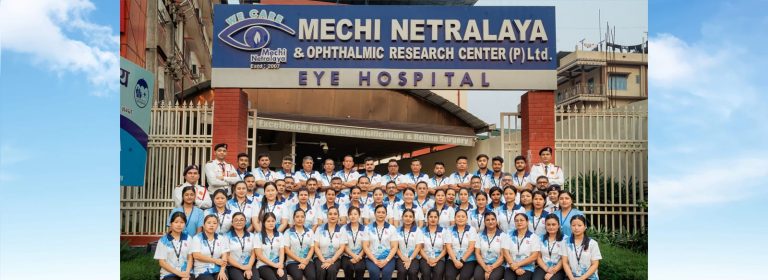 Group of people in uniform standing in front of Mechi Netralaya eye hospital sign