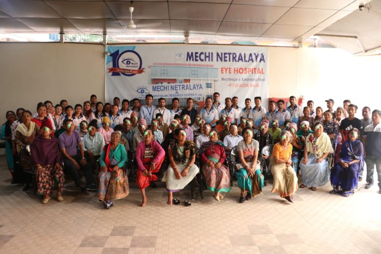 Group of people with eye patches posing in front of Mechi Netralaya banner